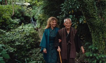 Movie still from “Until the End of the World” (1991), directed by Wim Wenders – An older man and a younger woman walking through the woods; Medium shot, Low angle