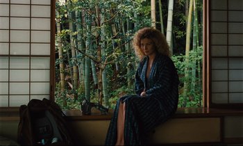 Movie still from “Until the End of the World” (1991), directed by Wim Wenders – A woman sitting on a window sill in front of a window; Wide shot, High angle