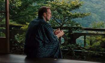 Movie still from “Until the End of the World” (1991), directed by Wim Wenders – A man sitting on top of a wooden bench; Wide shot, Over the shoulder angle