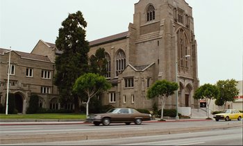 Movie still from “Until the End of the World” (1991), directed by Wim Wenders – A car driving down a street past a large church; Extreme Wide shot, Low angle