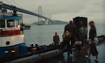 Movie still from “Until the End of the World” (1991), directed by Wim Wenders – Two men walking on a dock near a river; Wide shot, Low angle