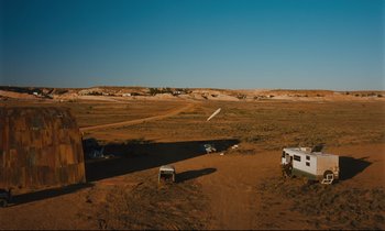 Movie still from “Until the End of the World” (1991), directed by Wim Wenders – An empty field with a white truck parked in the middle of it; Extreme Wide shot, High angle