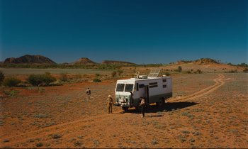Movie still from “Until the End of the World” (1991), directed by Wim Wenders – Two men standing next to an rv in the middle of a desert; Extreme Wide shot, High angle