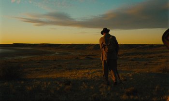Movie still from “Until the End of the World” (1991), directed by Wim Wenders – A man standing in the middle of an open field at sunset; Extreme Wide shot, Over the shoulder angle