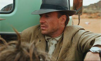 Movie still from “Until the End of the World” (1991), directed by Wim Wenders – A person wearing a suit and a hat; Close Up shot, Over the shoulder angle