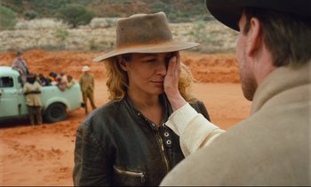 Movie still from “Until the End of the World” (1991), directed by Wim Wenders – A man touching a woman's face while standing on a dirt field; Close Up shot, Over the shoulder angle