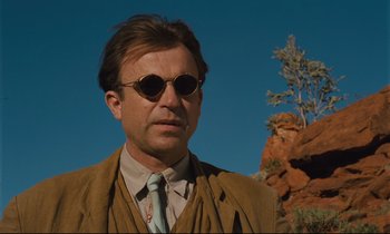 Movie still from “Until the End of the World” (1991), directed by Wim Wenders – A man wearing a suit and tie standing in front of a tree; Close Up shot, Low angle