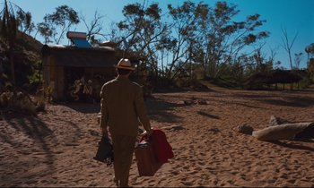 Movie still from “Until the End of the World” (1991), directed by Wim Wenders – A man walking on the beach with a bunch of luggage; Wide shot, High angle