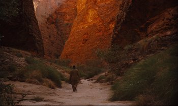 Movie still from “Until the End of the World” (1991), directed by Wim Wenders – A person is walking down a trail in the mountains; Extreme Wide shot, High angle