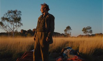 Movie still from “Until the End of the World” (1991), directed by Wim Wenders – A man standing in a field near some grass; Wide shot, Low angle