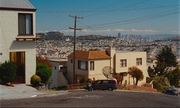 Movie still from “Until the End of the World” (1991), directed by Wim Wenders – A car parked on the side of the road in front of a house; Extreme Wide shot, High angle