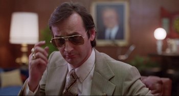 Movie still from “Used Cars” (1980), directed by Robert Zemeckis – A man in a suit and tie wearing sunglasses; Close Up shot, Low angle