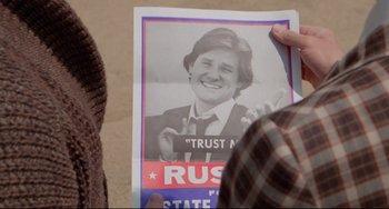 Movie still from “Used Cars” (1980), directed by Robert Zemeckis – A person holding up a poster with a picture of a man; Close Up shot, High angle