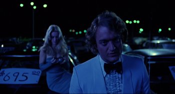 Movie still from “Used Cars” (1980), directed by Robert Zemeckis – A man and a woman in formal wear in a car lot at night; Medium shot, Over the shoulder angle