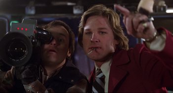 Movie still from “Used Cars” (1980), directed by Robert Zemeckis – A man with a cigarette in his mouth and another man in a red jacket; Medium shot, Low angle