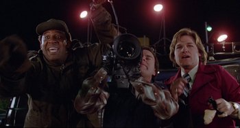 Movie still from “Used Cars” (1980), directed by Robert Zemeckis – A group of people standing around a camera; Medium shot, Low angle