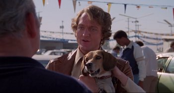 Movie still from “Used Cars” (1980), directed by Robert Zemeckis – A man holding a brown and white dog in his arms; Close Up shot, Over the shoulder angle