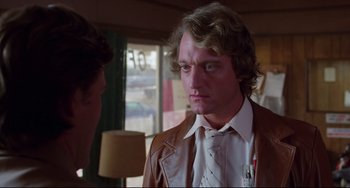 Movie still from “Used Cars” (1980), directed by Robert Zemeckis – A man in a brown leather jacket and a white shirt is talking to another man in a brown leather jacket; Close Up shot, Over the shoulder angle