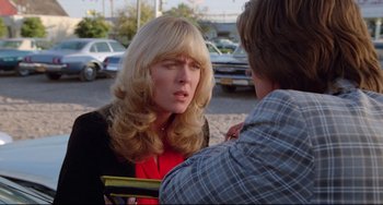 Movie still from “Used Cars” (1980), directed by Robert Zemeckis – A woman with long blonde hair talking to a man in a parking lot; Close Up shot, Over the shoulder angle