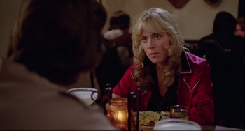 Movie still from “Used Cars” (1980), directed by Robert Zemeckis – A woman sitting at a table with a plate of food in front of her; Close Up shot, Over the shoulder angle