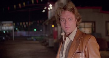 Movie still from “Used Cars” (1980), directed by Robert Zemeckis – A man in a brown jacket is standing in a parking lot at night; Close Up shot, Low angle