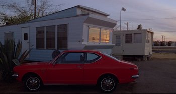 Movie still from “Used Cars” (1980), directed by Robert Zemeckis – A red car parked in front of a trailer home; Wide shot, Low angle