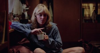 Movie still from “Used Cars” (1980), directed by Robert Zemeckis – A woman sitting on a couch holding a cup of coffee; Medium shot, Low angle