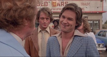 Movie still from “Used Cars” (1980), directed by Robert Zemeckis – A group of men standing next to each other in a parking lot; Close Up shot, Over the shoulder angle