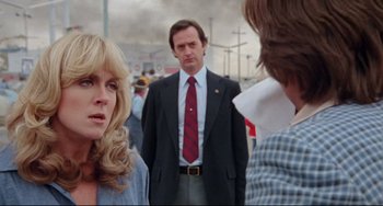 Movie still from “Used Cars” (1980), directed by Robert Zemeckis – A man in a suit and tie standing next to a woman; Close Up shot, Over the shoulder angle