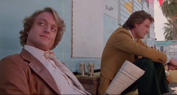 Movie still from “Used Cars” (1980), directed by Robert Zemeckis – A man sitting next to another man in a room; Medium shot, Low angle