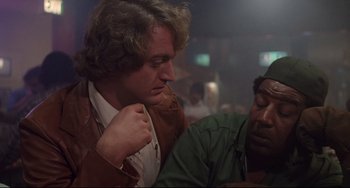 Movie still from “Used Cars” (1980), directed by Robert Zemeckis – A man putting on a jacket next to another man; Close Up shot, Over the shoulder angle