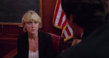 Movie still from “Used Cars” (1980), directed by Robert Zemeckis – A woman sitting in front of an american flag in a courtroom; Close Up shot, Over the shoulder angle