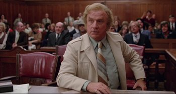 Movie still from “Used Cars” (1980), directed by Robert Zemeckis – A man sitting at a table in front of a crowd; Medium shot, Low angle