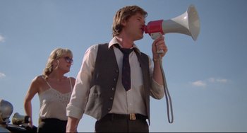 Movie still from “Used Cars” (1980), directed by Robert Zemeckis – A man with a megaphone and a woman; Medium shot, Low angle