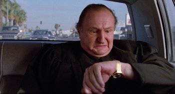 Movie still from “Used Cars” (1980), directed by Robert Zemeckis – An older man looking at his watch while sitting in the back of a car; Medium shot, Low angle
