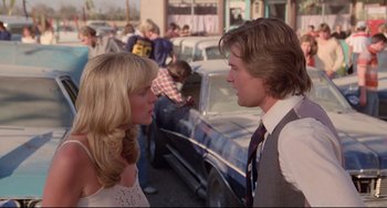 Movie still from “Used Cars” (1980), directed by Robert Zemeckis – A man and a woman talking in front of a car; Medium shot, Over the shoulder angle