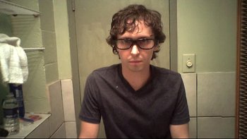 Movie still from “V/H/S” (2012), directed by Joe Swanberg – A young man wearing glasses in a bathroom; Close Up shot, Overhead angle