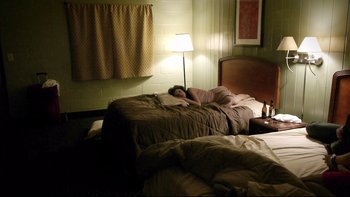 Movie still from “V/H/S” (2012), directed by Joe Swanberg – A person sleeping in a bed in a hotel room; Wide shot, High angle
