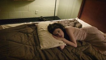 Movie still from “V/H/S” (2012), directed by Joe Swanberg – A woman laying on a bed with a pillow; Medium shot, Overhead angle