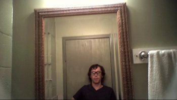 Movie still from “V/H/S” (2012), directed by Joe Swanberg – A man standing in front of a mirror in a room; Medium shot, Overhead angle