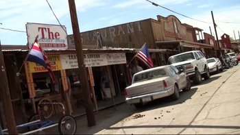 Movie still from “V/H/S” (2012), directed by Joe Swanberg – An image of an old western town with a car parked in front of it; Wide shot, High angle