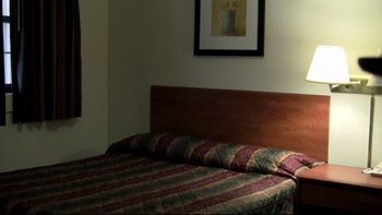 Movie still from “V/H/S” (2012), directed by Joe Swanberg – A bed with a wooden headboard in a room; Wide shot, High angle