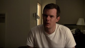 Movie still from “V/H/S” (2012), directed by Joe Swanberg – A man in a white t - shirt is sitting in front of a window; Close Up shot, Low angle