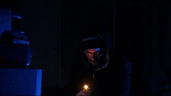 Movie still from “V/H/S” (2012), directed by Joe Swanberg – A man holding a lit candle in a dark room; Medium shot, Low angle