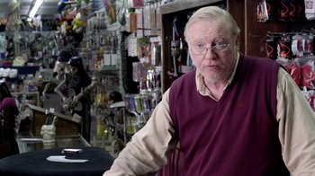 Movie still from “V/H/S Viral” (2014), directed by Aaron Moorhead – An older man standing in front of a table; Medium shot, Over the shoulder angle