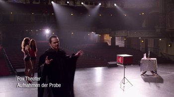 Movie still from “V/H/S Viral” (2014), directed by Aaron Moorhead – A man in a black robe stands in front of an empty stage; Extreme Wide shot, High angle