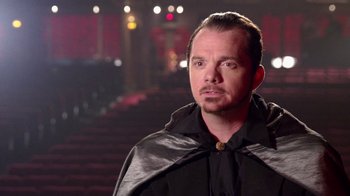 Movie still from “V/H/S Viral” (2014), directed by Aaron Moorhead – A man wearing a black cape in front of a stage; Close Up shot, Over the shoulder angle