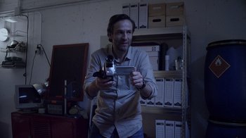 Movie still from “V/H/S Viral” (2014), directed by Aaron Moorhead – A man holding a camera in a room with shelves; Medium shot, High angle