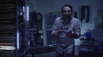 Movie still from “V/H/S Viral” (2014), directed by Aaron Moorhead – A man is holding a video camera in a dark room; Medium shot, Low angle
