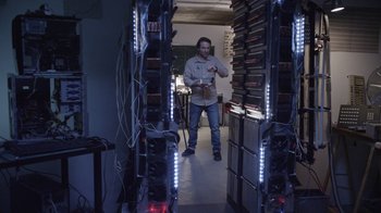 Movie still from “V/H/S Viral” (2014), directed by Aaron Moorhead – A man standing in front of a room filled with stacks of computer equipment; Wide shot, Low angle